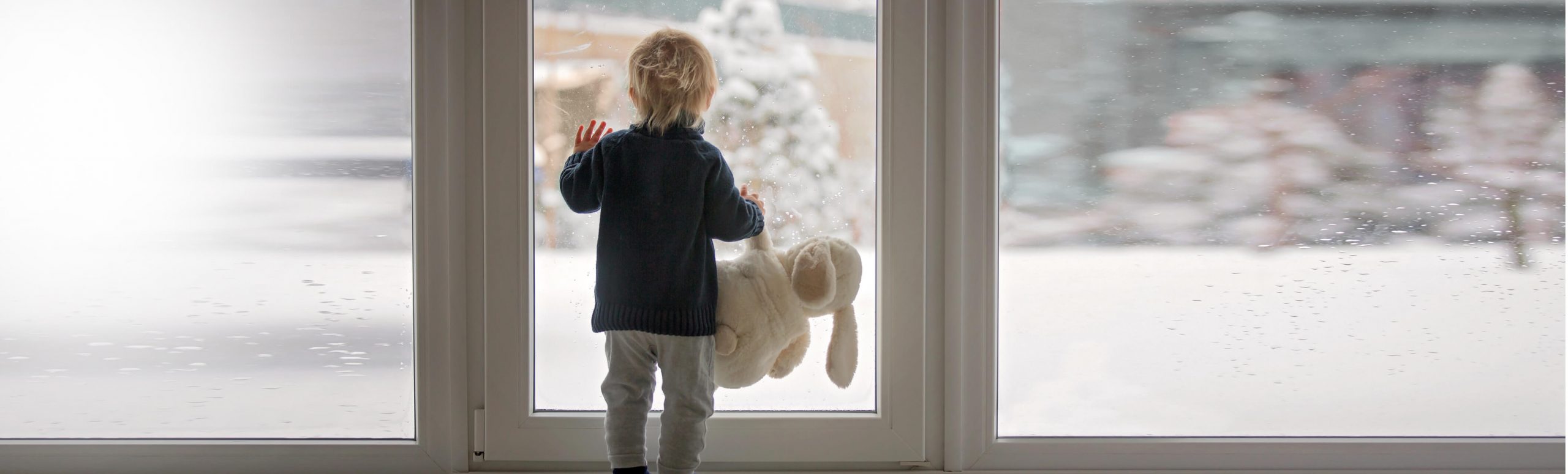 幼儿抱着泰迪熊看着窗外的雪