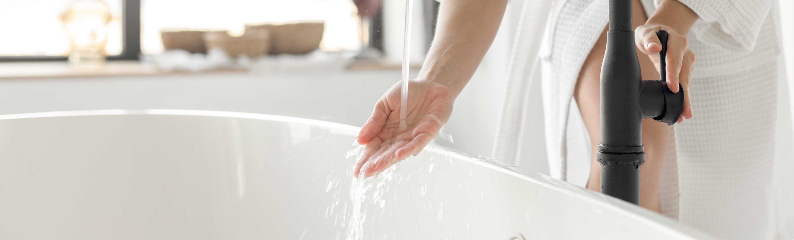 女人的手检查水温从水龙头超过浴缸