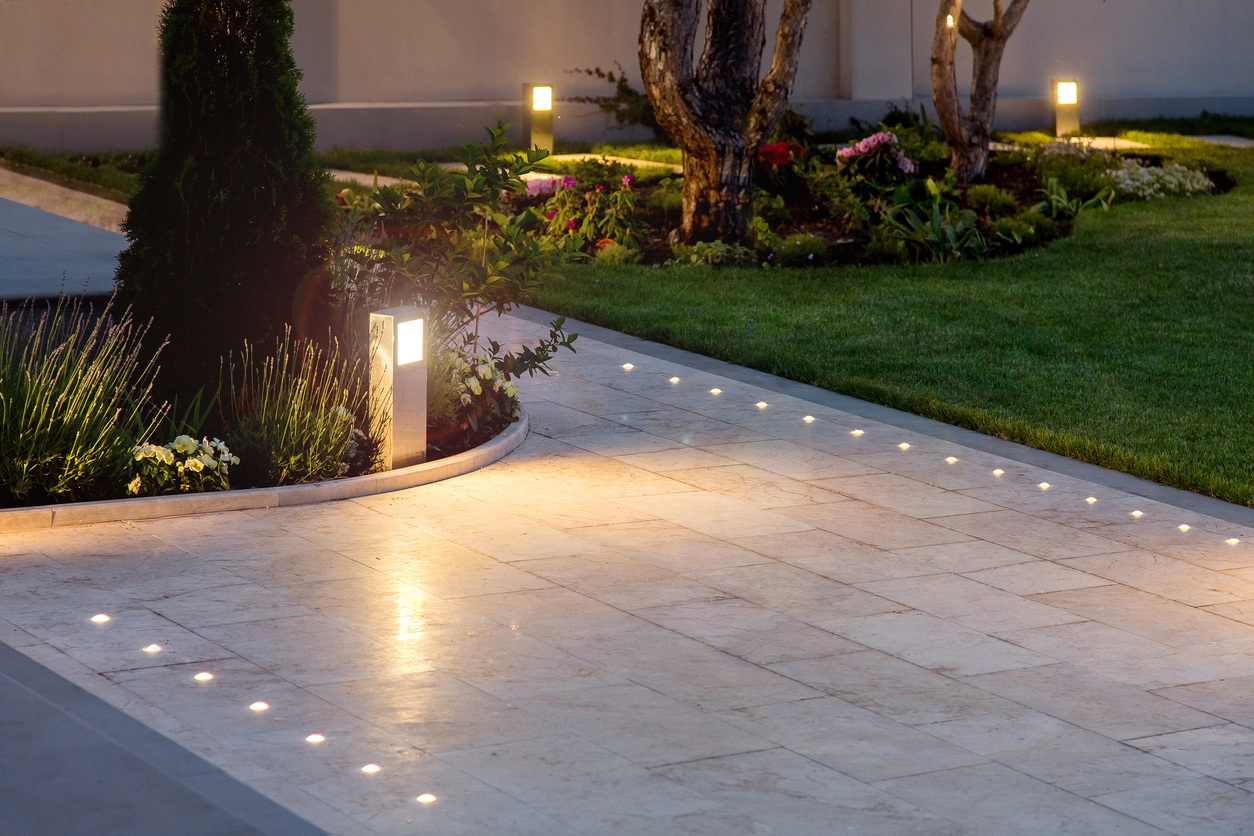 大理石瓷砖游乐场在夜晚后院的豪宅花坛和草坪与地面灯和照明在温暖的光线在傍晚。